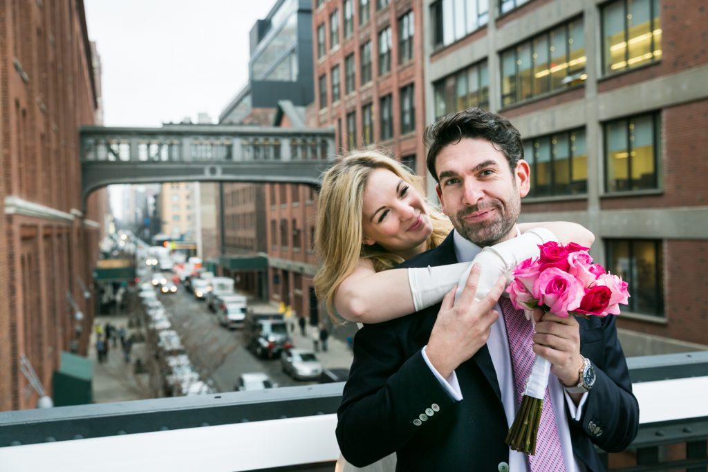 Bride hugging groom from behind on the High Line with view of NYC street in background