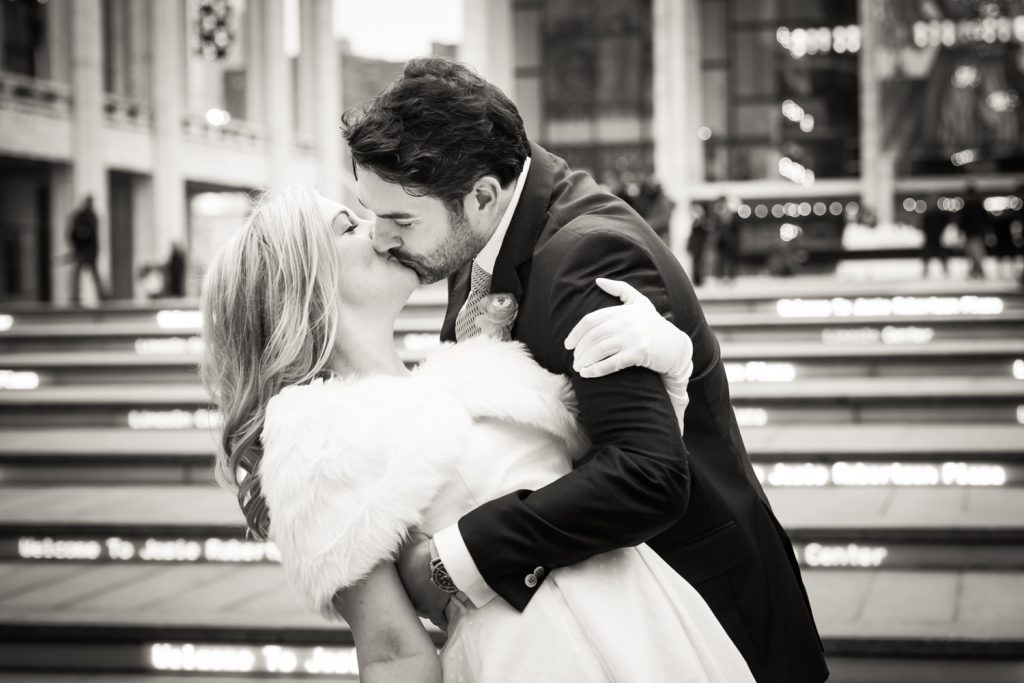 Black and white photo of bride and groom kissing on the steps of Lincoln Center