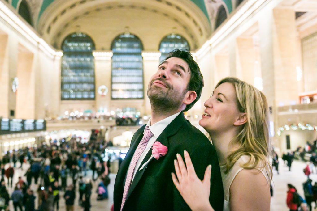 Bride hugging groom from behind in Grand Central Terminal main concourse