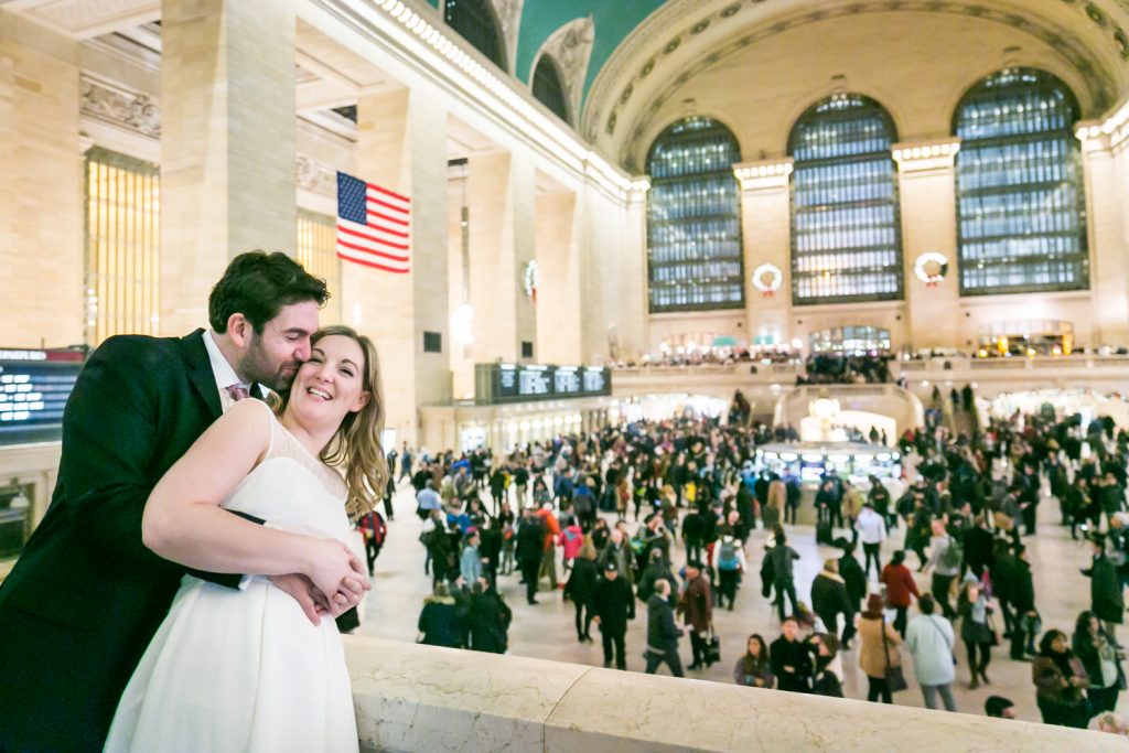 Groom hugging bride with view of Grand Central Terminal main concourse