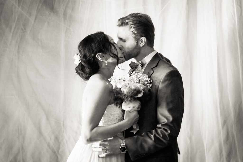 Black and white photo of bride and groom kissing after ceremony