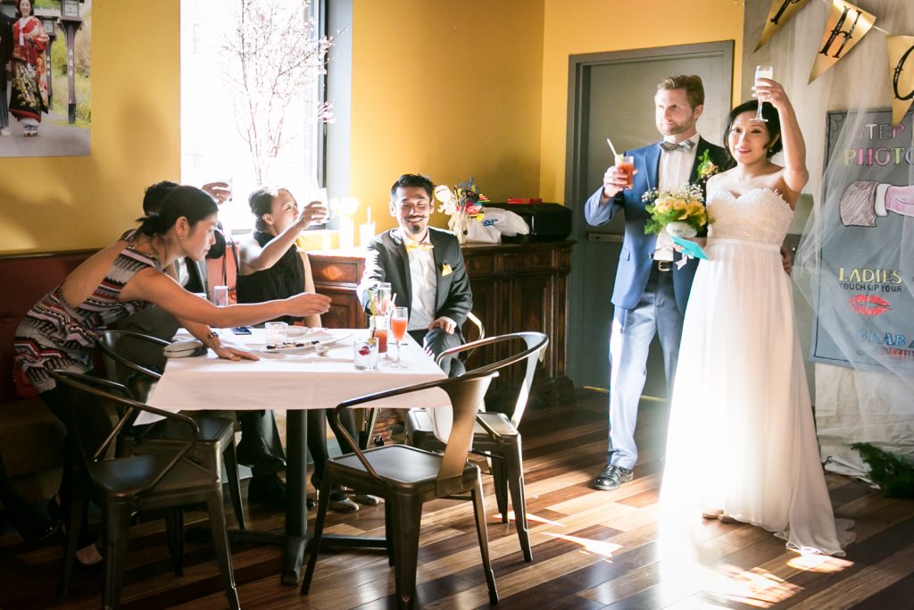 Bride and groom raising glasses with guests at an Astoria restaurant wedding