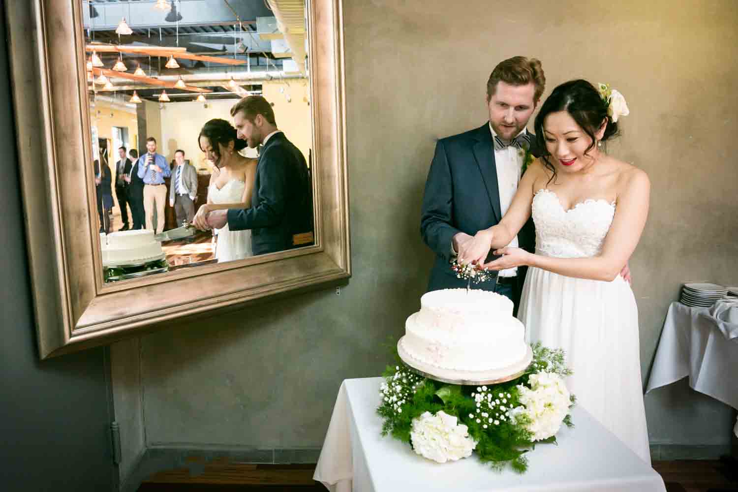 Bride and groom cutting cake with reflection in mirror