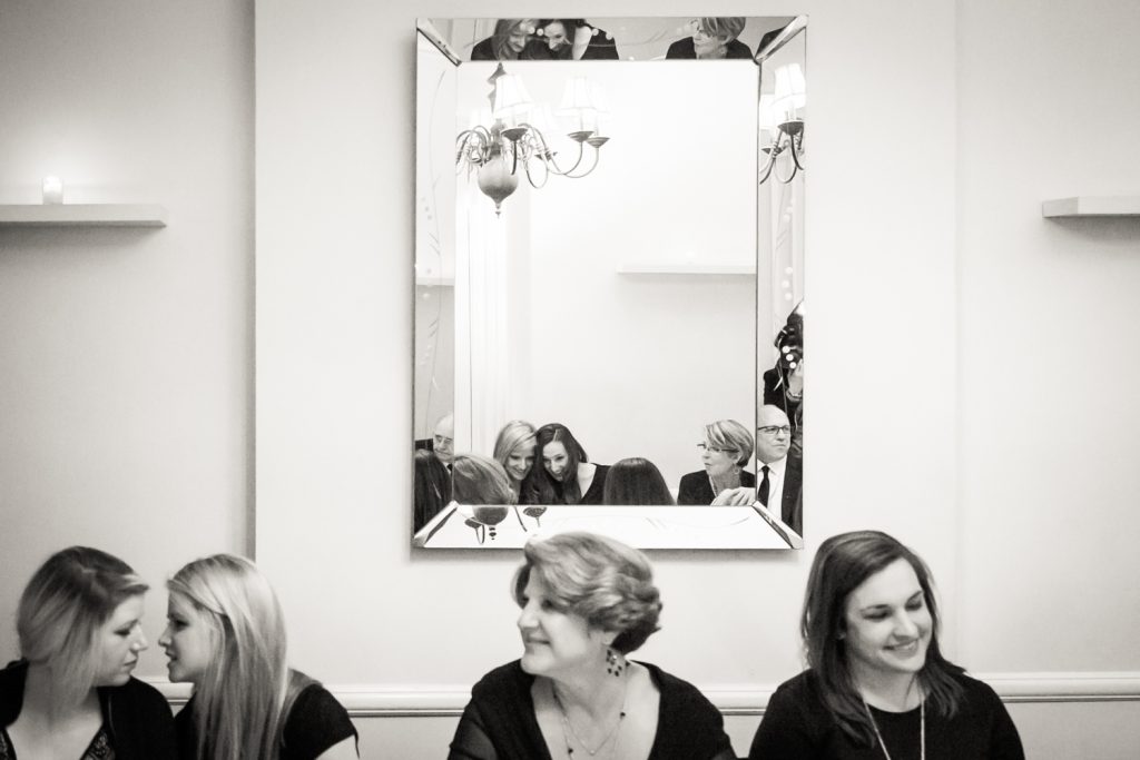 Black and white photo of guests talking and reflected in mirror