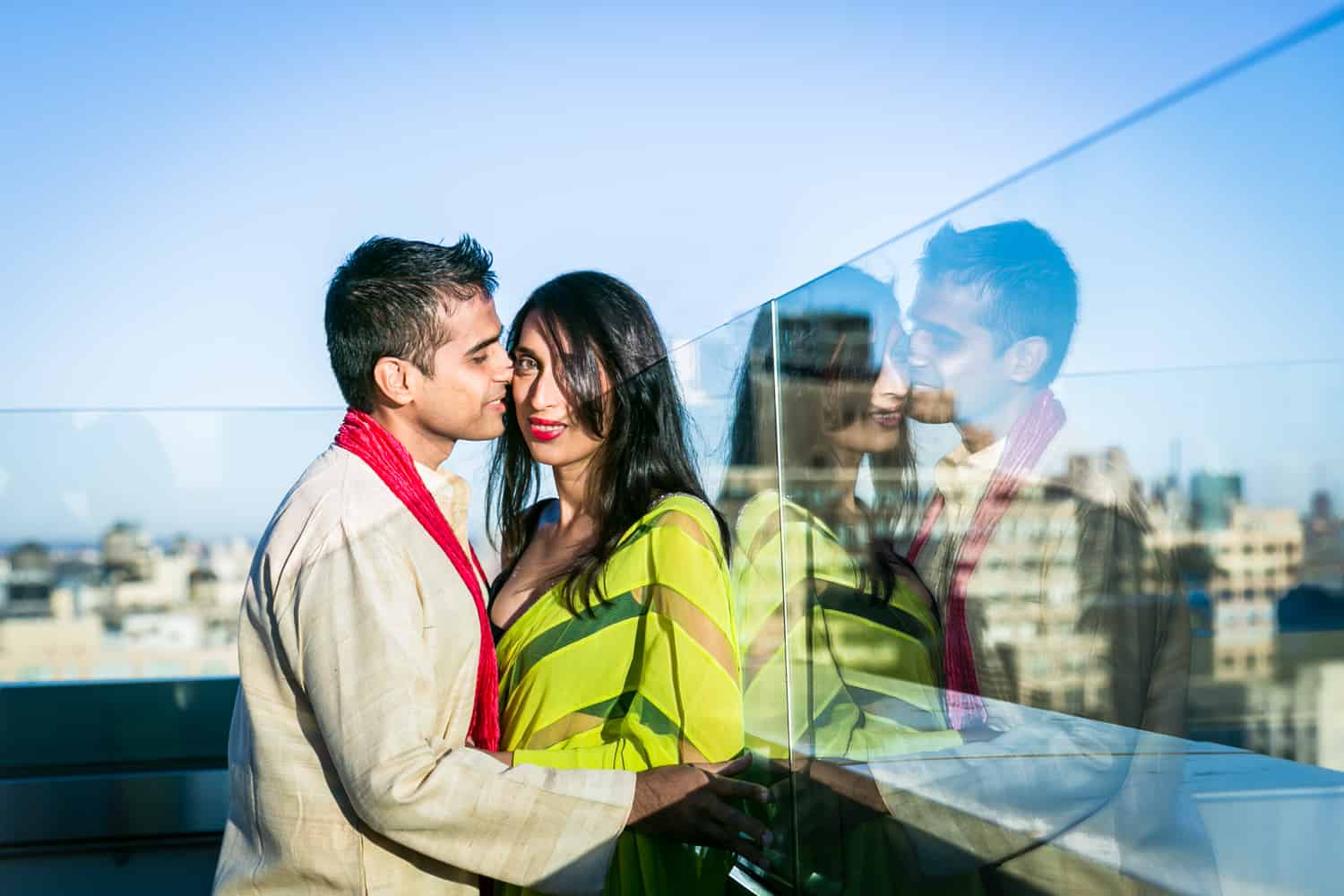 Engaged couple on rooftop wearing traditional Indian attire with reflection in glass wall