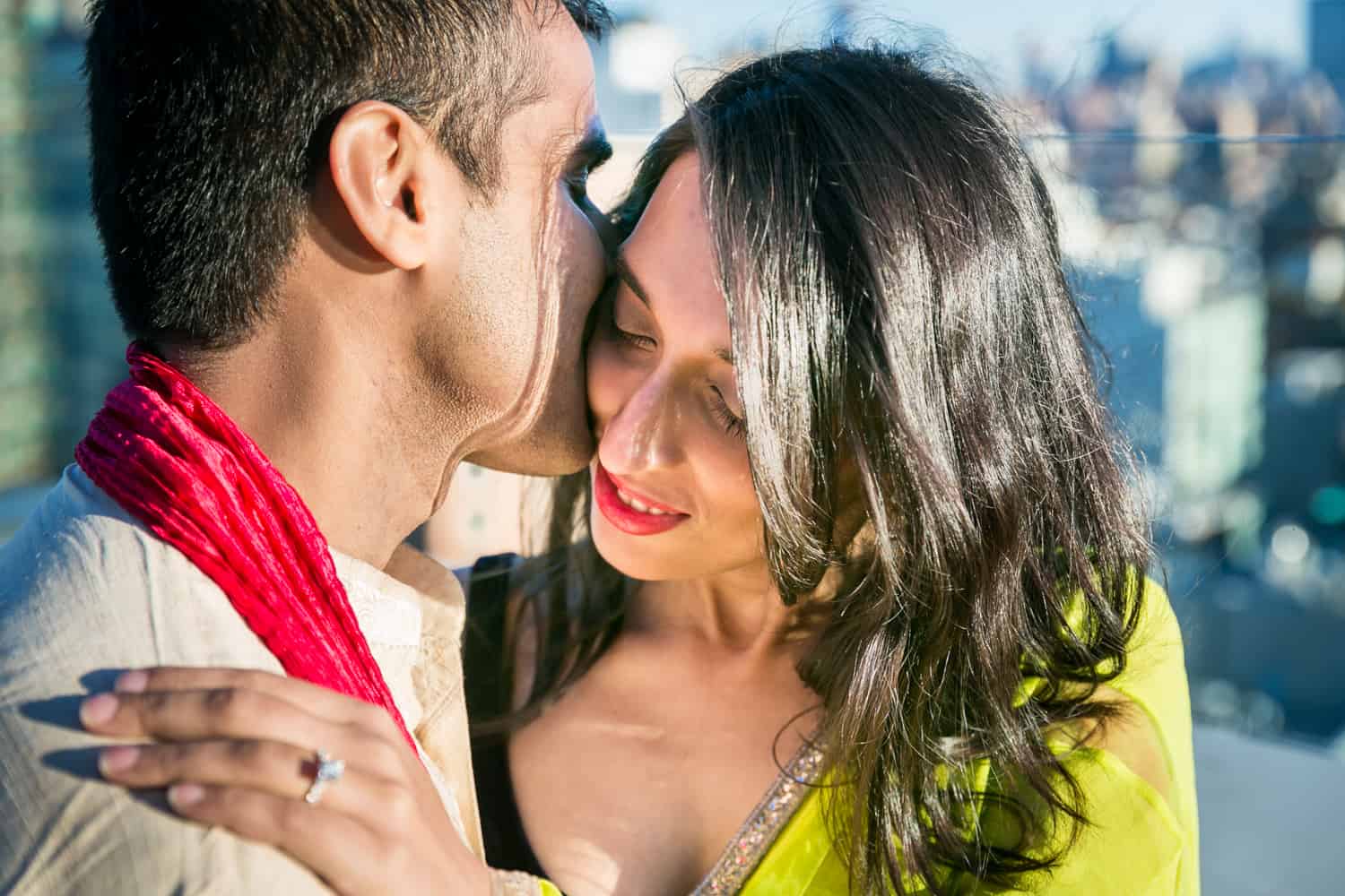 Couple wearing traditional Indian attire and man kissing woman on side of head