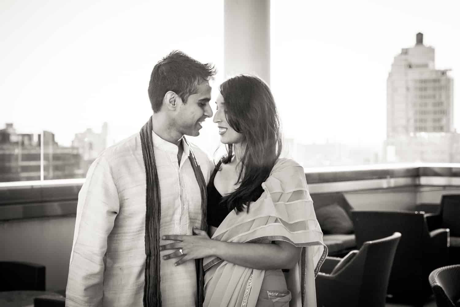 Black and white photo of engaged couple on rooftop wearing traditional Indian attire