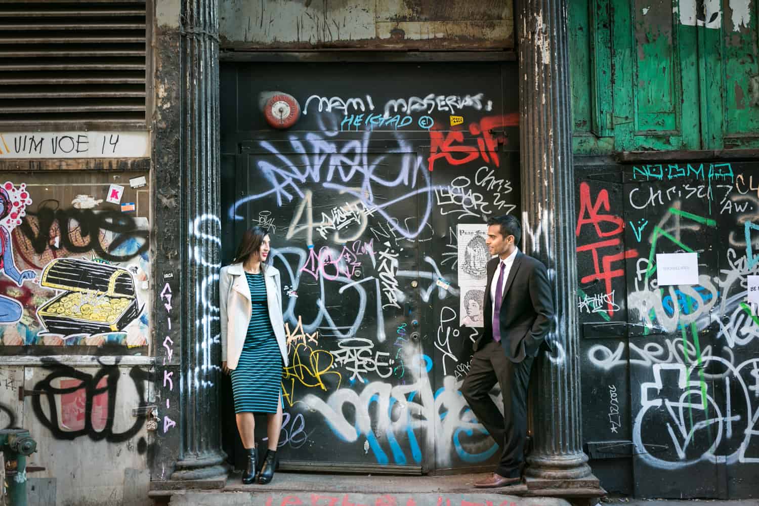Couple leaning separately against columns of graffiti-covered wall for an article entitled,' How I get clients comfortable in front of the camera' 