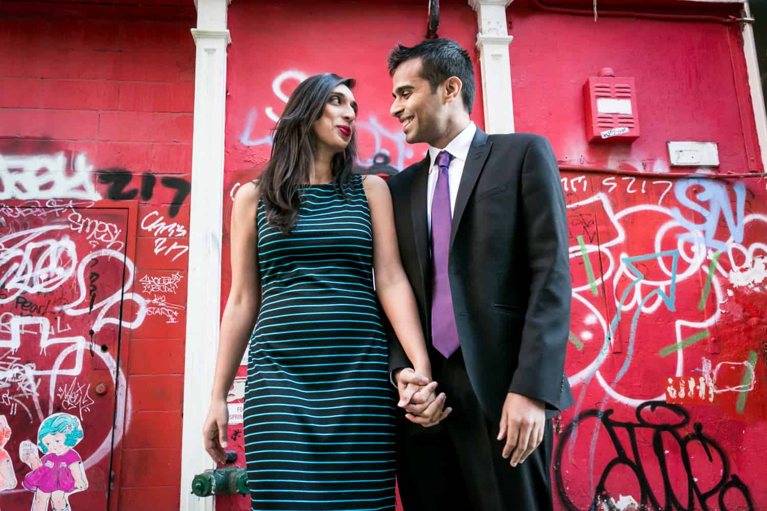 Couple holding hands in front of red graffiti wall in Tribeca