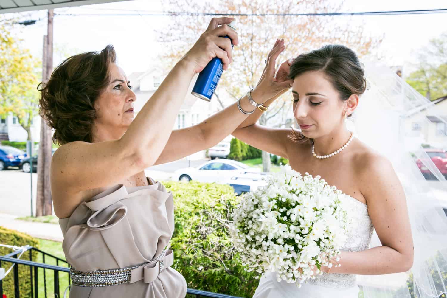 Mother spraying bride's hair with hairspray