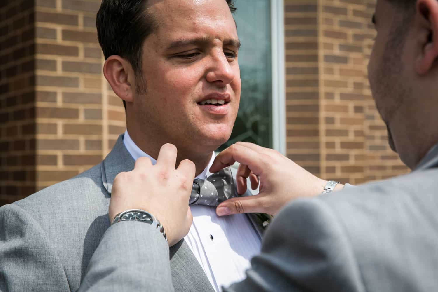Man's hands adjusting bowtie of groom for an article called 'Do you need a second photographer?'
