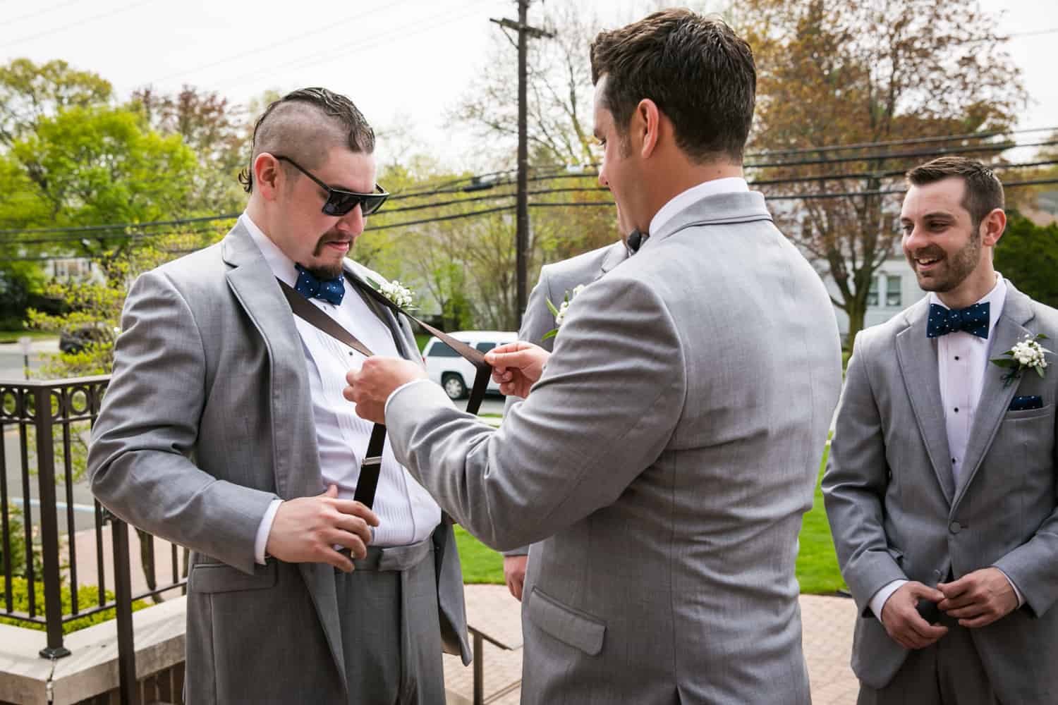 Groom snapping suspenders of groomsman wearing sunglasses