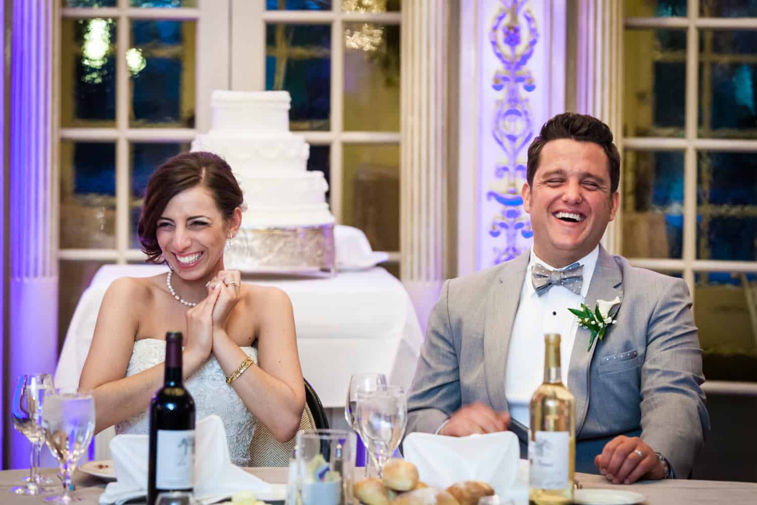 Bride and groom at sweetheart table laughing during speeches