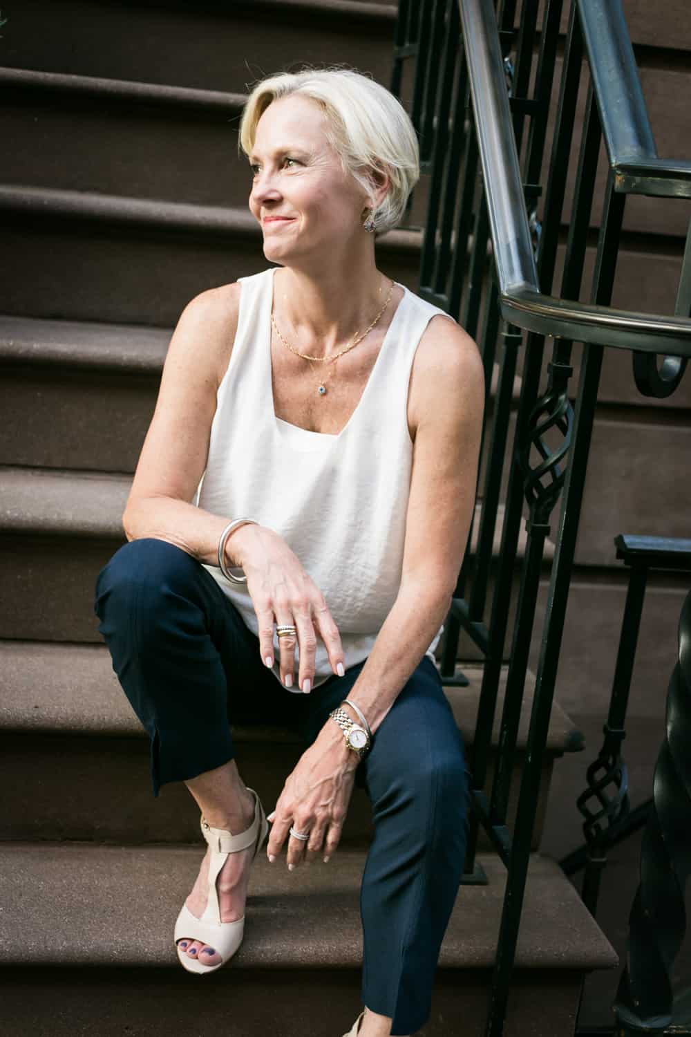 Older woman wearing white sleeveless top sitting on steps