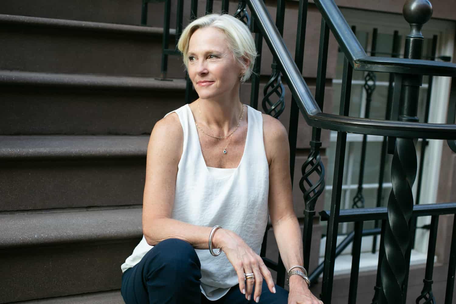 Older woman wearing white sleeveless top sitting on steps