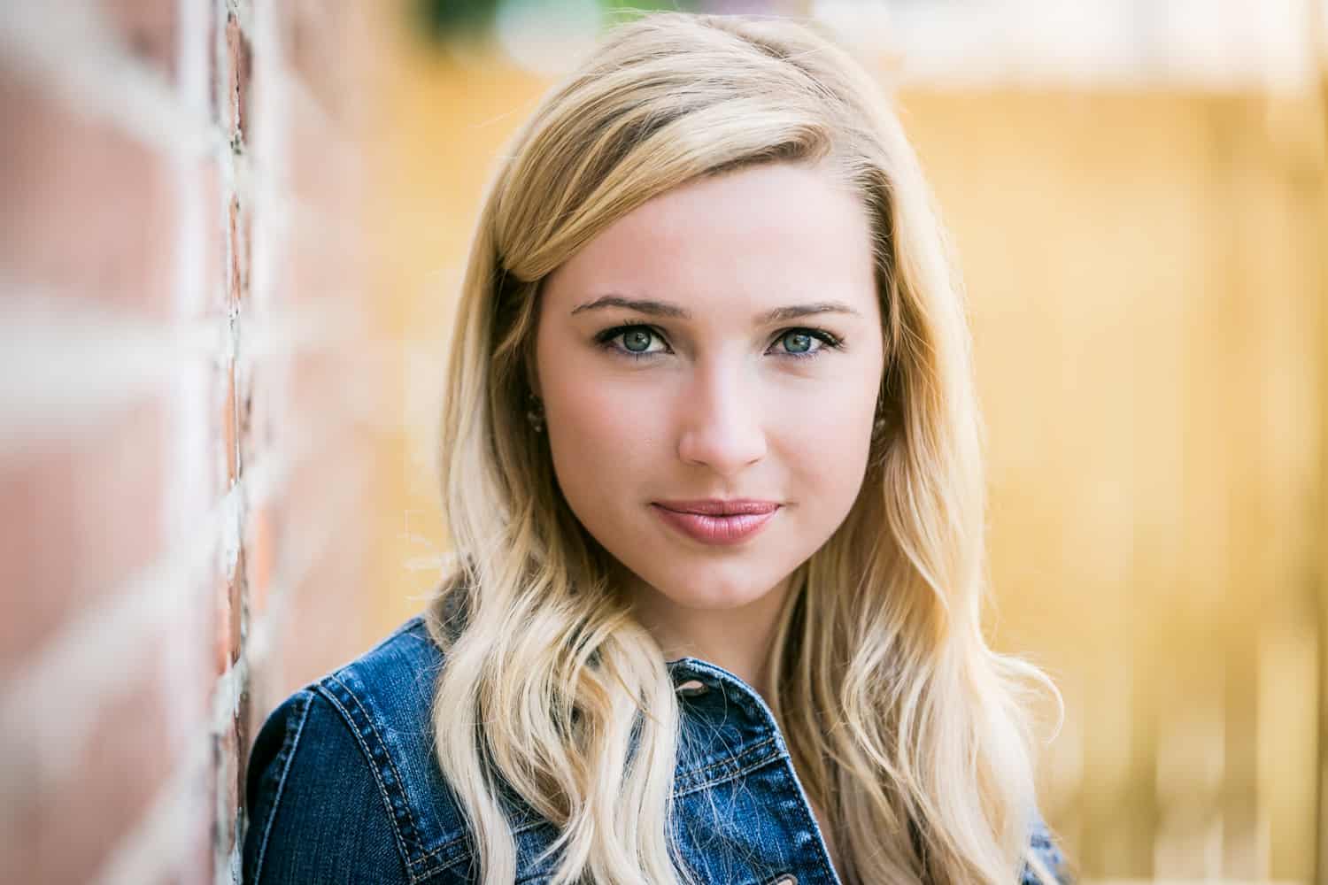 Non-smiling blond actress against brick wall