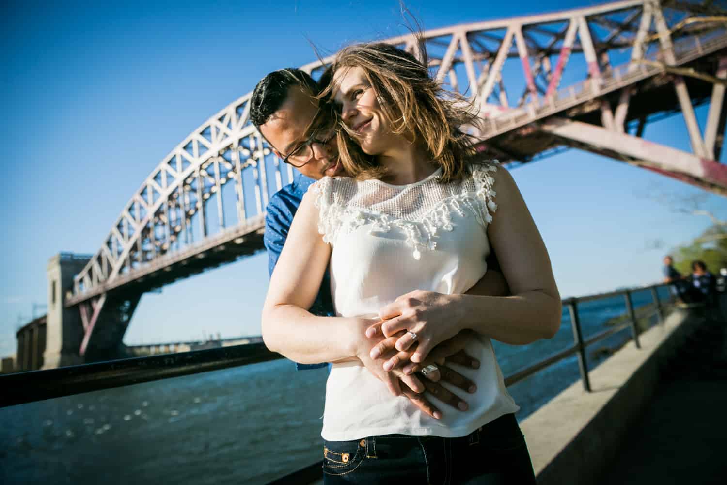 Couple hugging in front of Hellgate Bridge during an Astoria Park engagement shoot