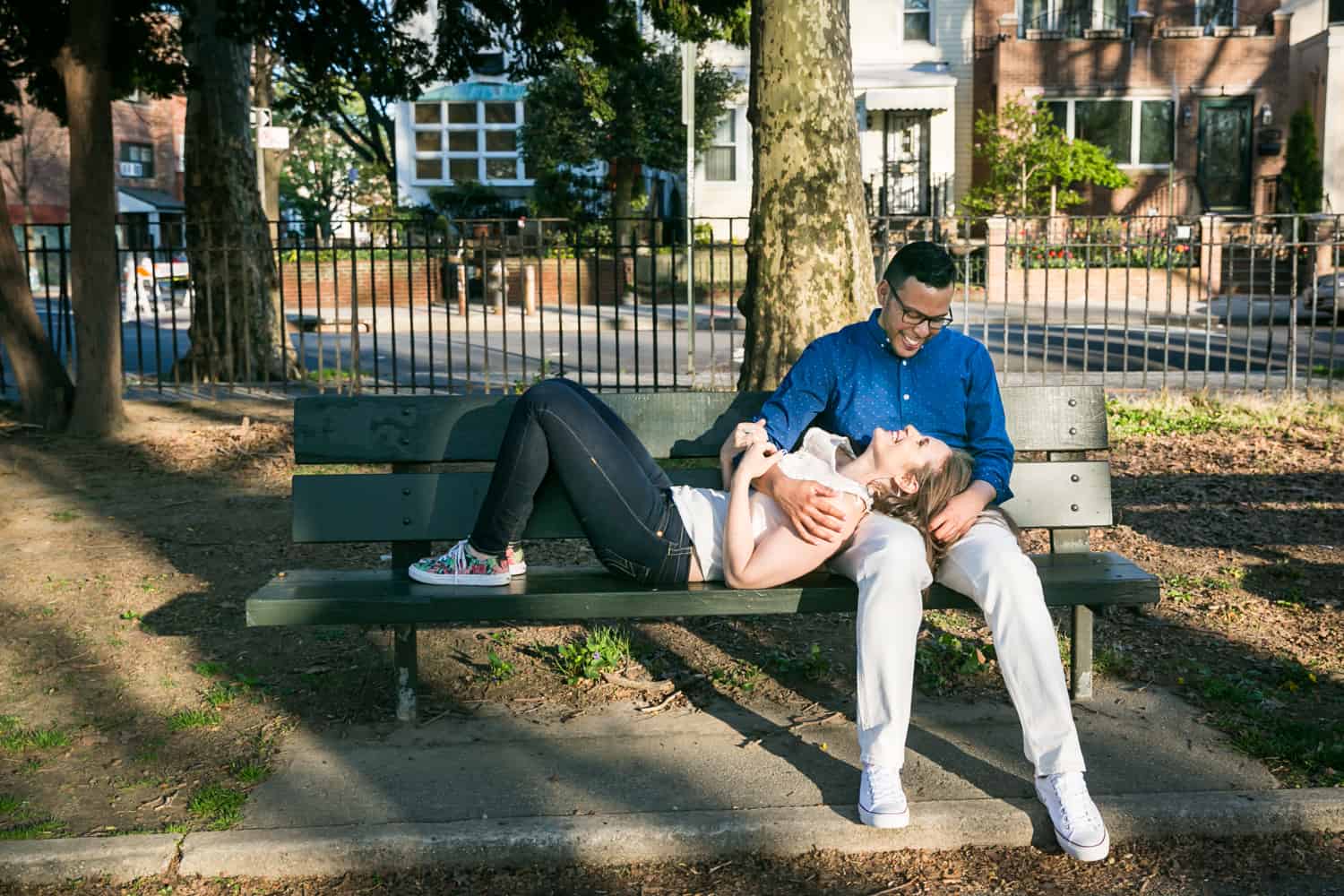 Woman lying in man's lap on bench during an Astoria Park engagement shoot