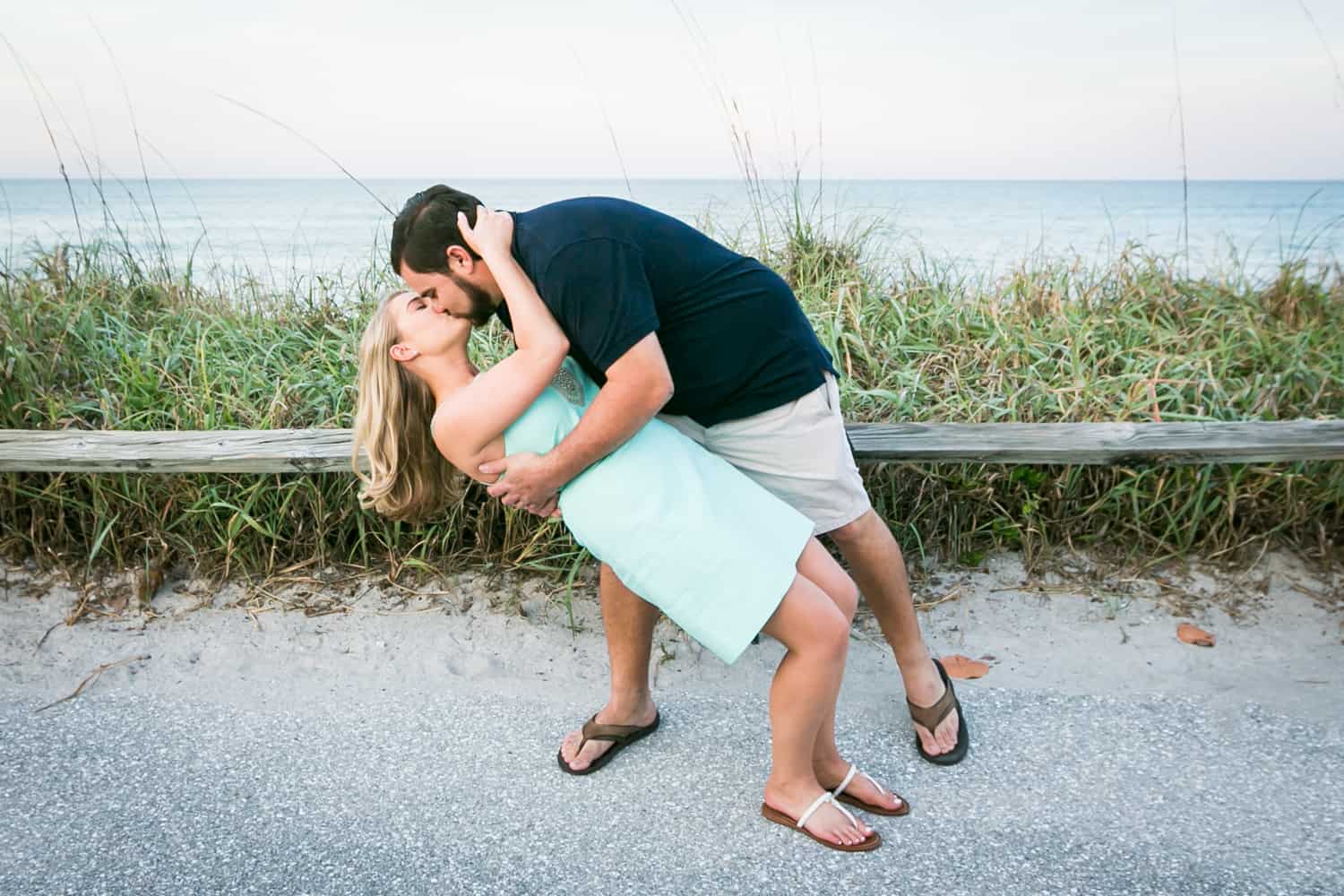 Man dipping woman and kissing her on beach during a Coral Cove Park engagement shoot