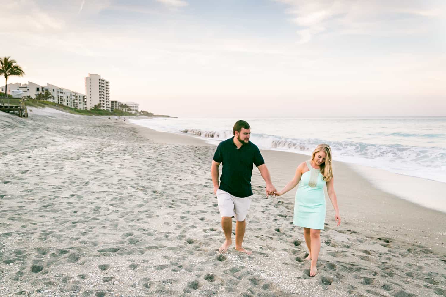 Couple holding hands and walking on beach during a Coral Cove Park engagement shoot