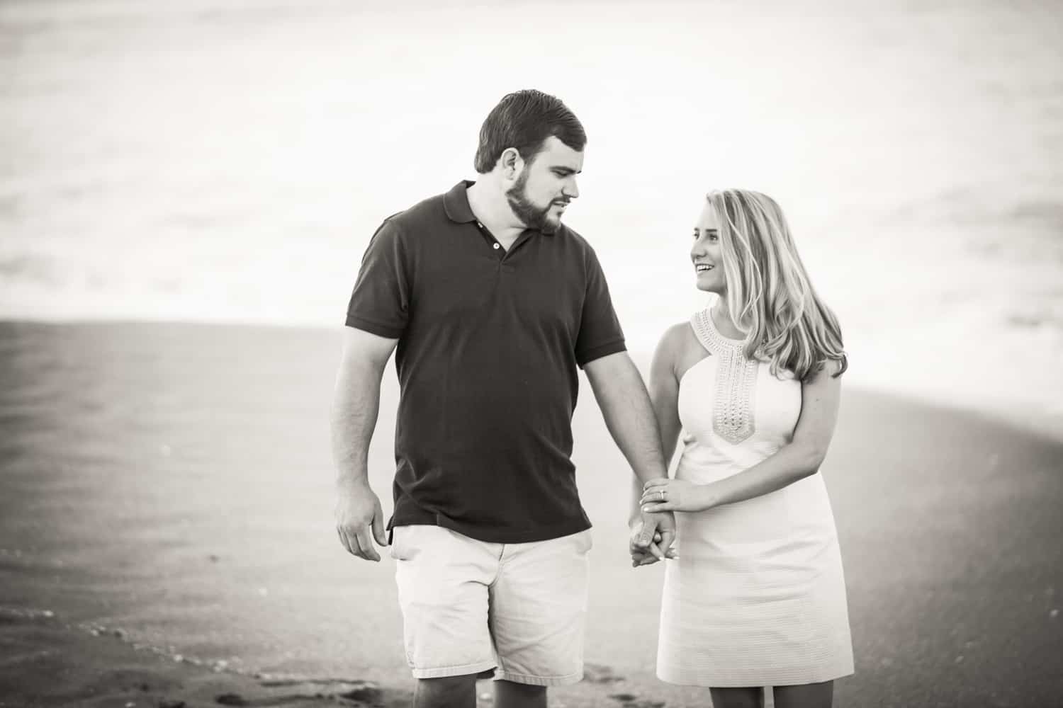 Black and white photo of couple holding hands on beach during a Coral Cove Park engagement shoot
