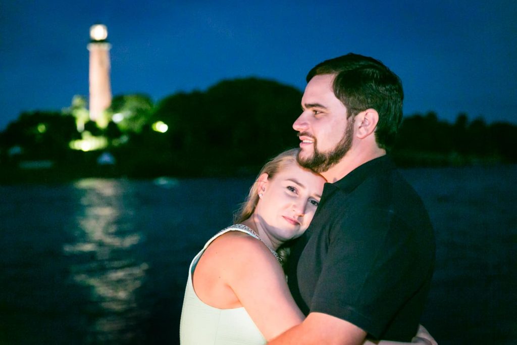 Couple hugging at night with lighthouse in background during a Coral Cove Park engagement shoot