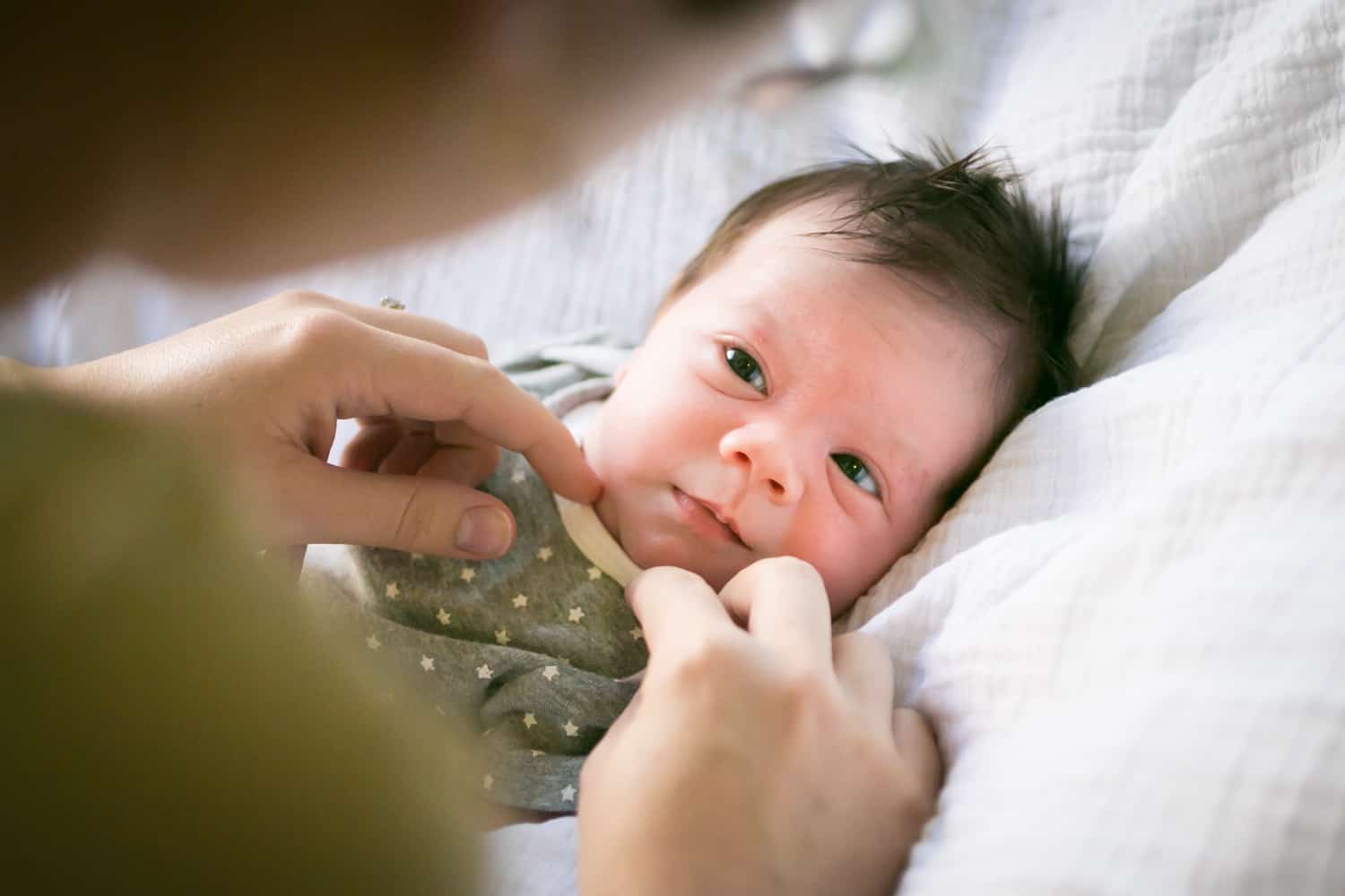 Newborn baby on white blanket for an article answering the question, 'is camera flash dangerous to newborns?'