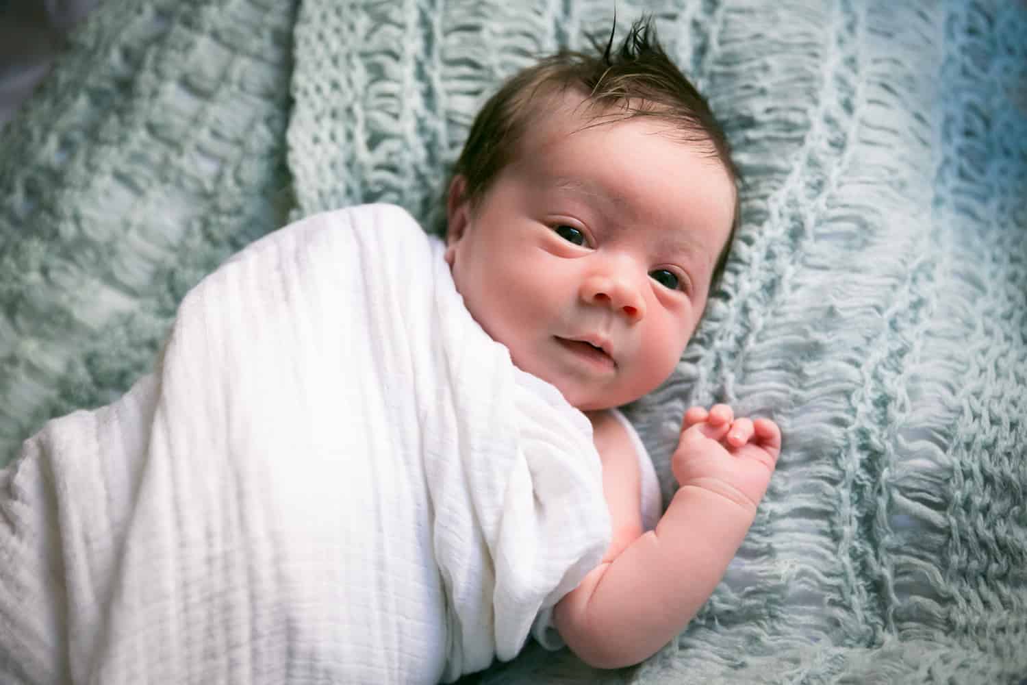 Newborn baby on blue blanket for an article answering the question, 'is camera flash dangerous to newborns?'