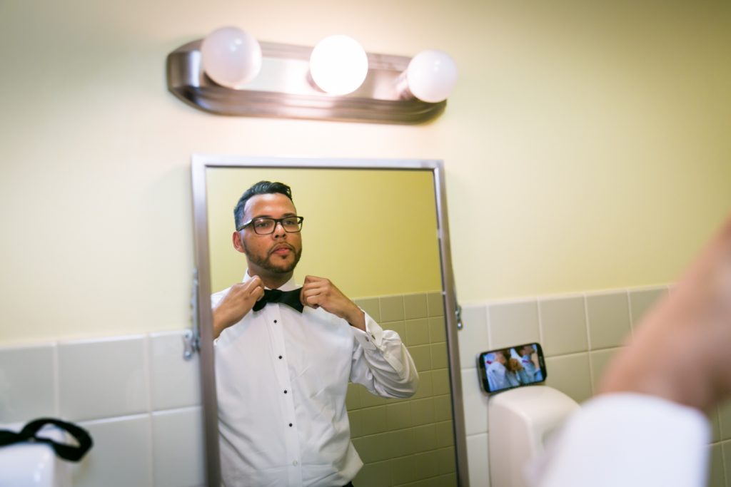 Groom adjusting bow tie in mirror before wedding