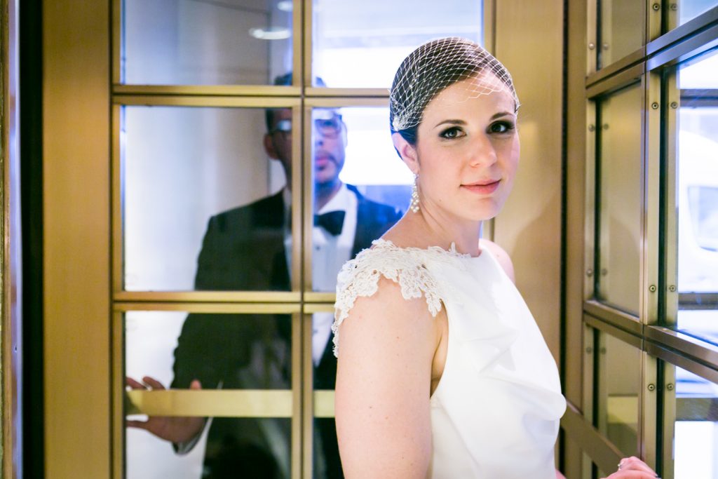 Bride with groom behind turnstile door in Roosevelt Hotel wedding photo