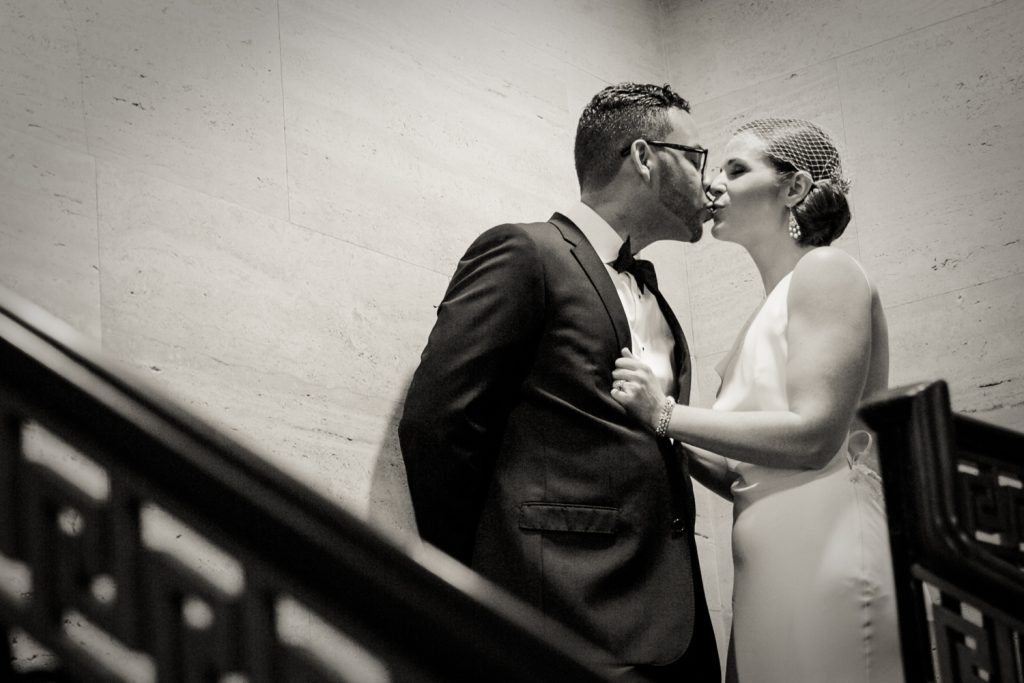 Black and white photo of bride and groom kissing in stairwell in Roosevelt Hotel wedding photo