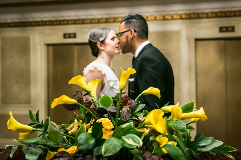View through yellow plant of bride and groom about to kiss in Roosevelt Hotel wedding photo