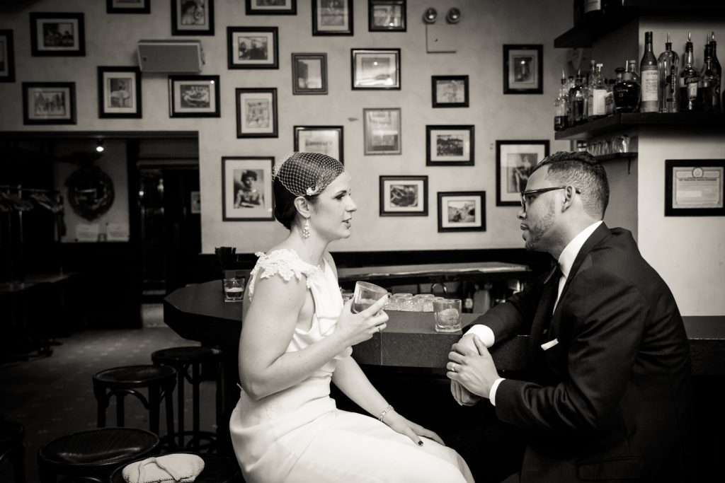 Black and white photo of bride and groom sitting at bar drinking