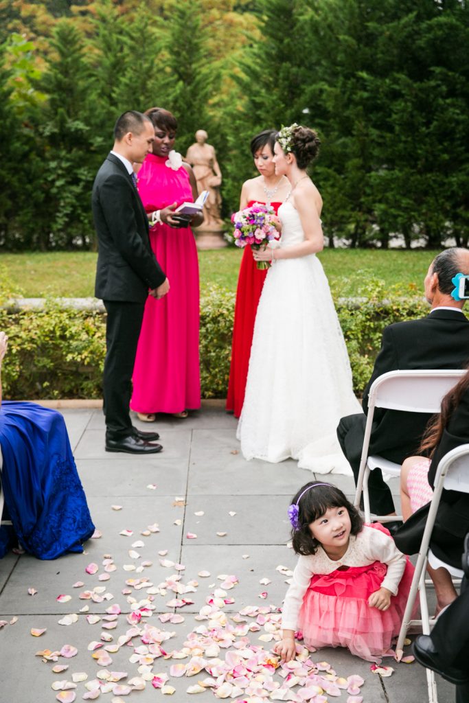 Bride and groom exchanging vows and little girl picking up flowers