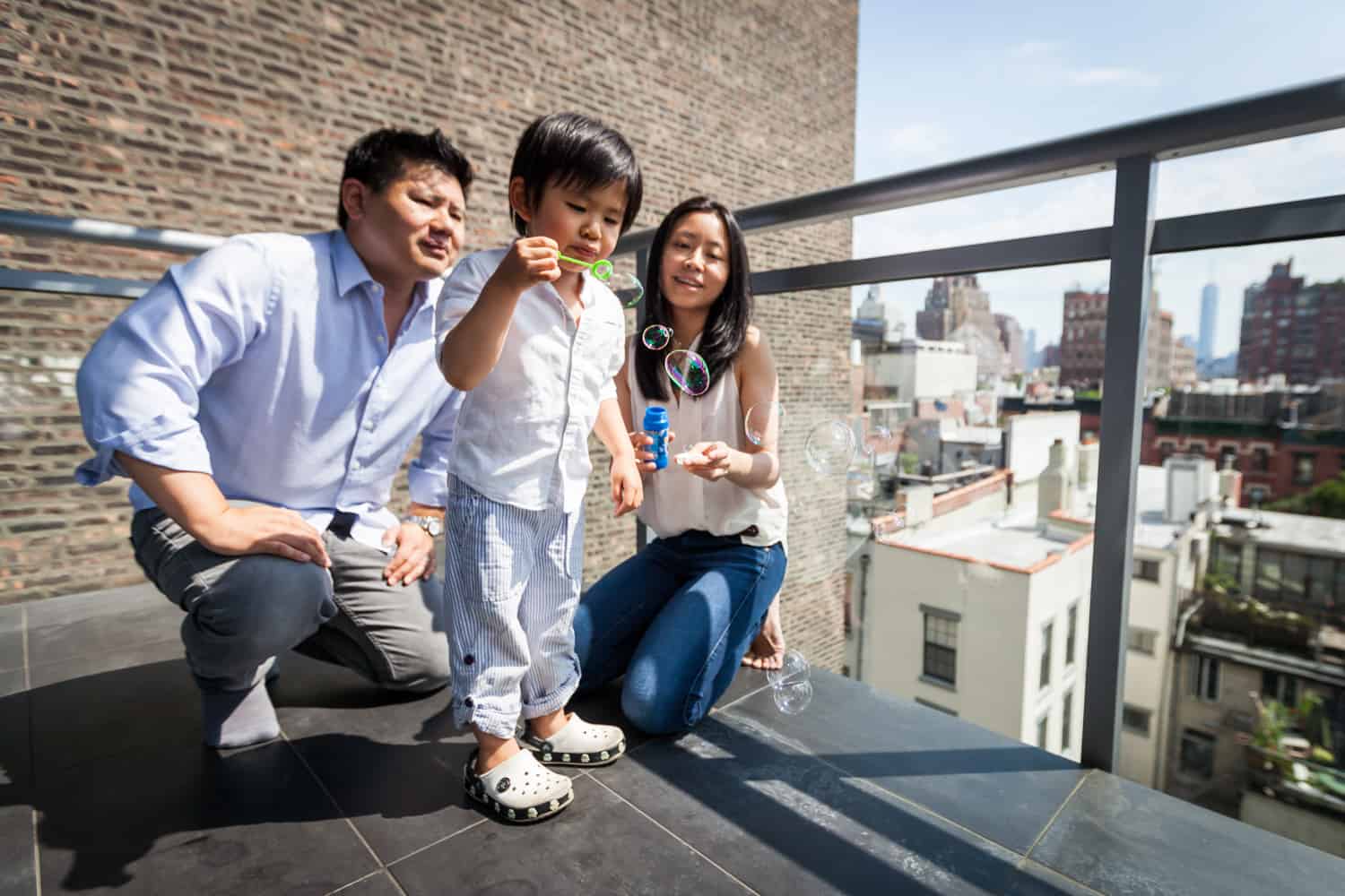 Chelsea family portrait of parents and little boy blowing bubbles on terrace
