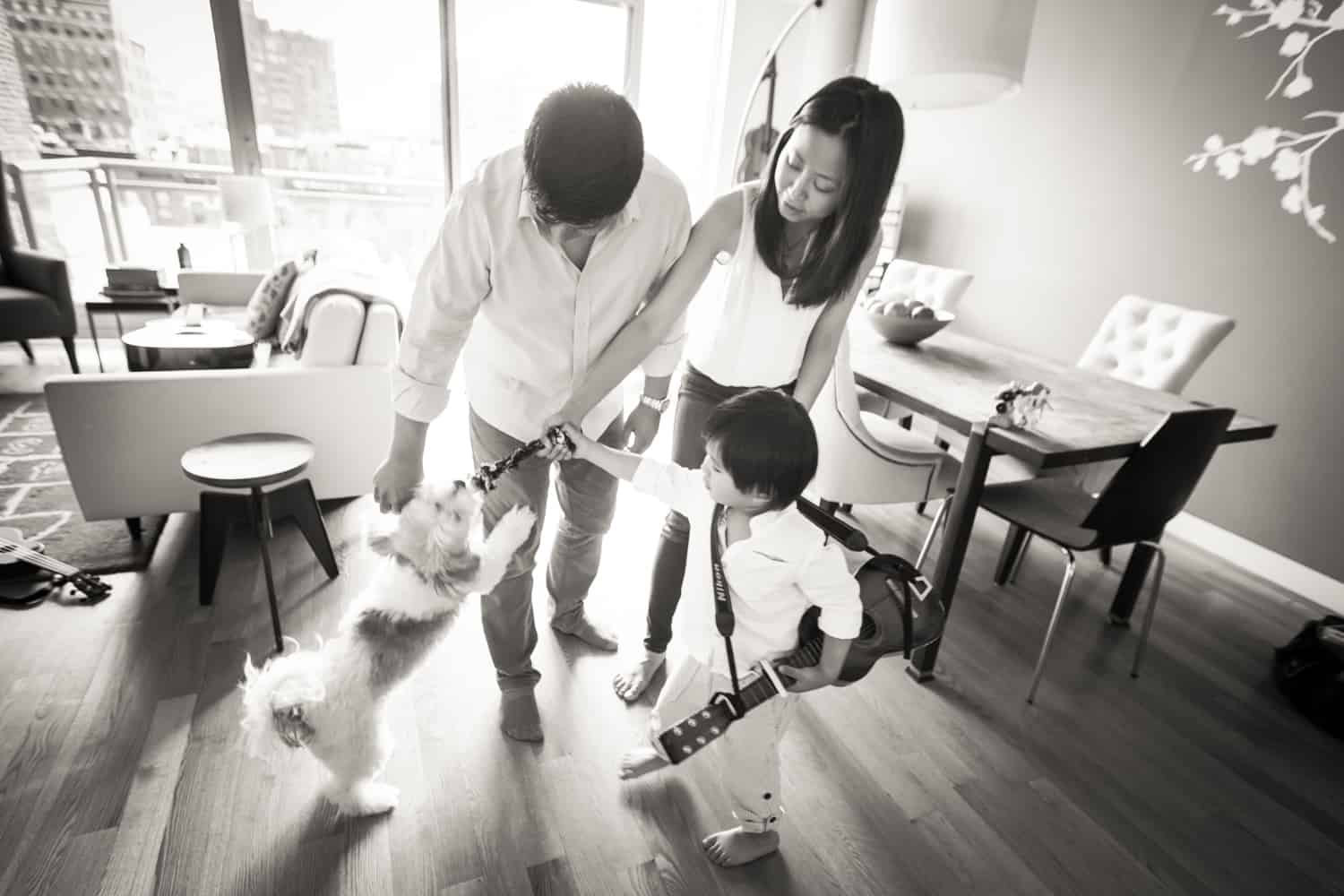 Black and white photo of parents and little boy playing with dog