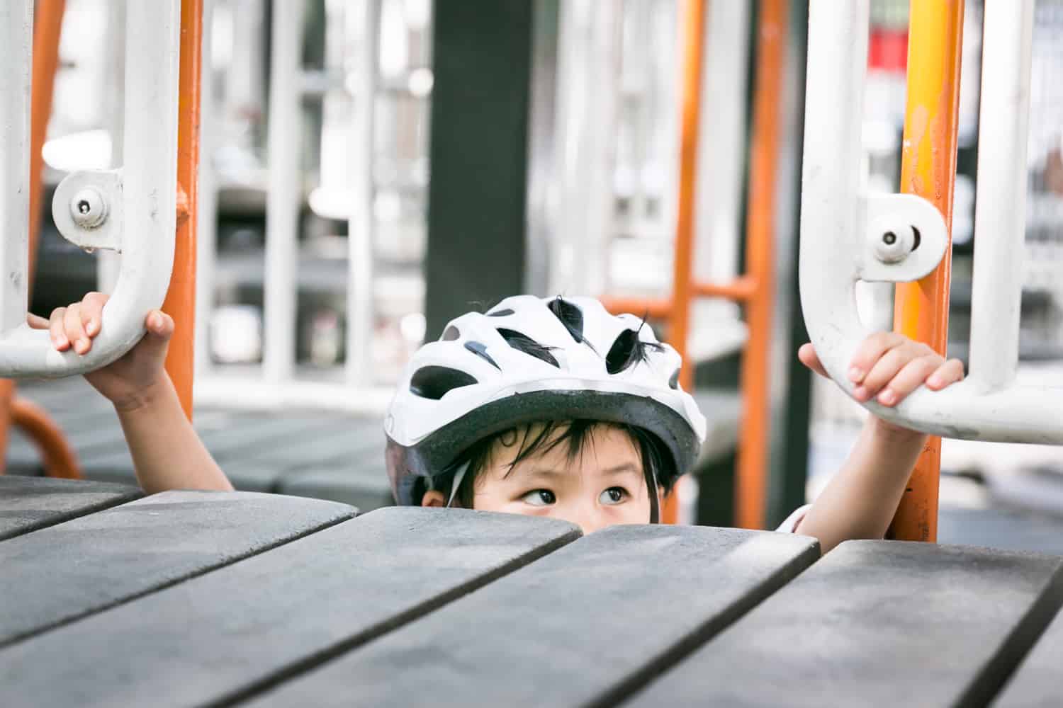Little boy wearing bike helmet peeking over edge of playground