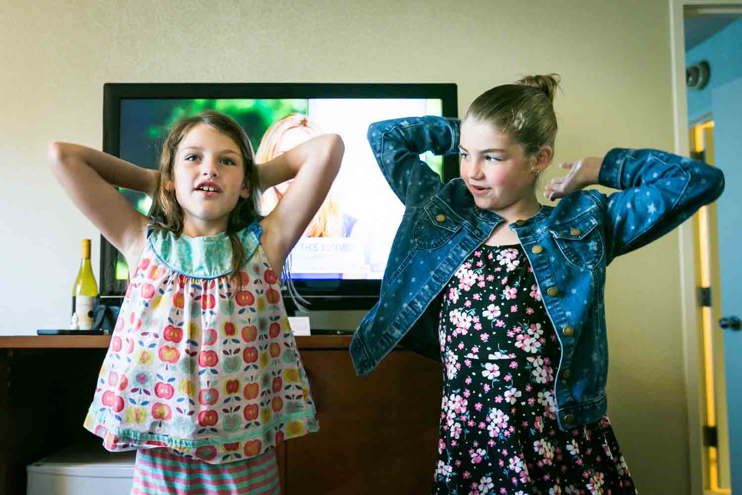 Two little girls dancing with arms up in a hotel room