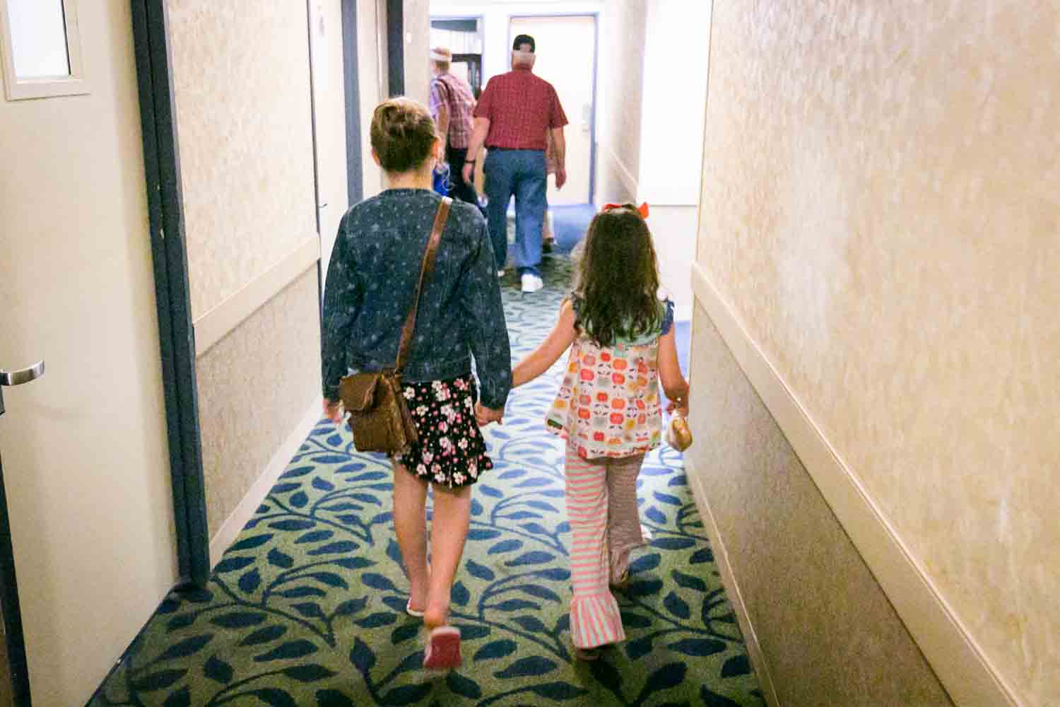 Two little girls holding hands walking down a hallway