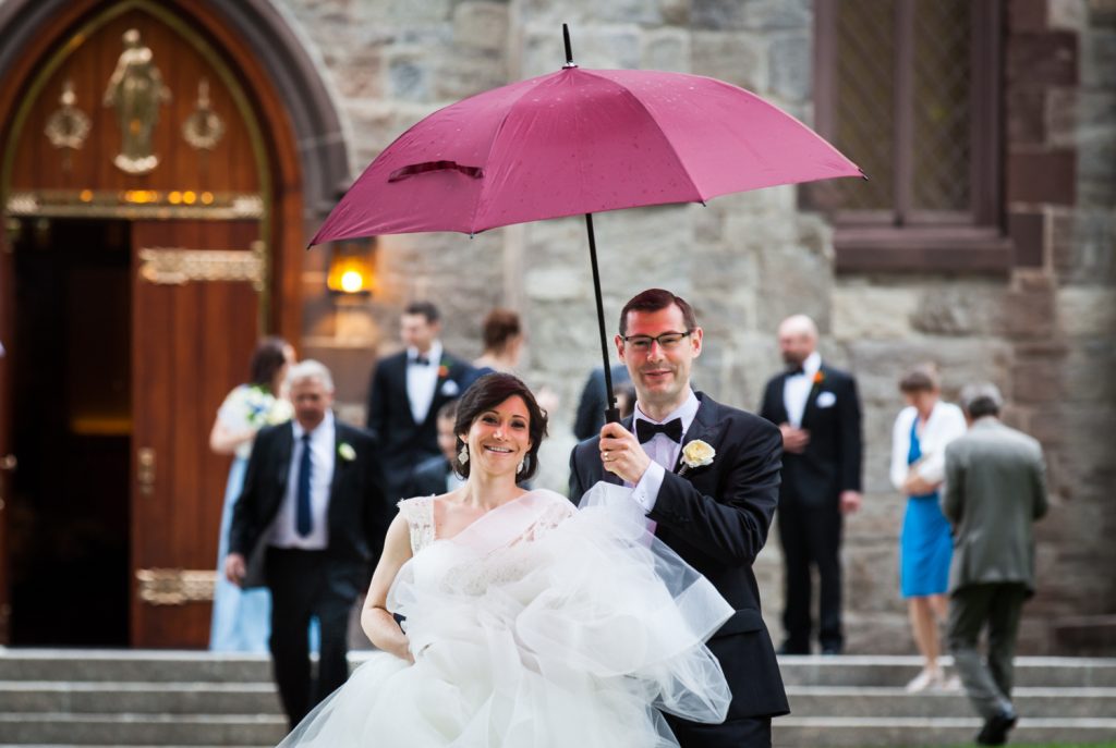 Bride and groom walking in rain under red umbrella for an article on NYC rainy day photo tips