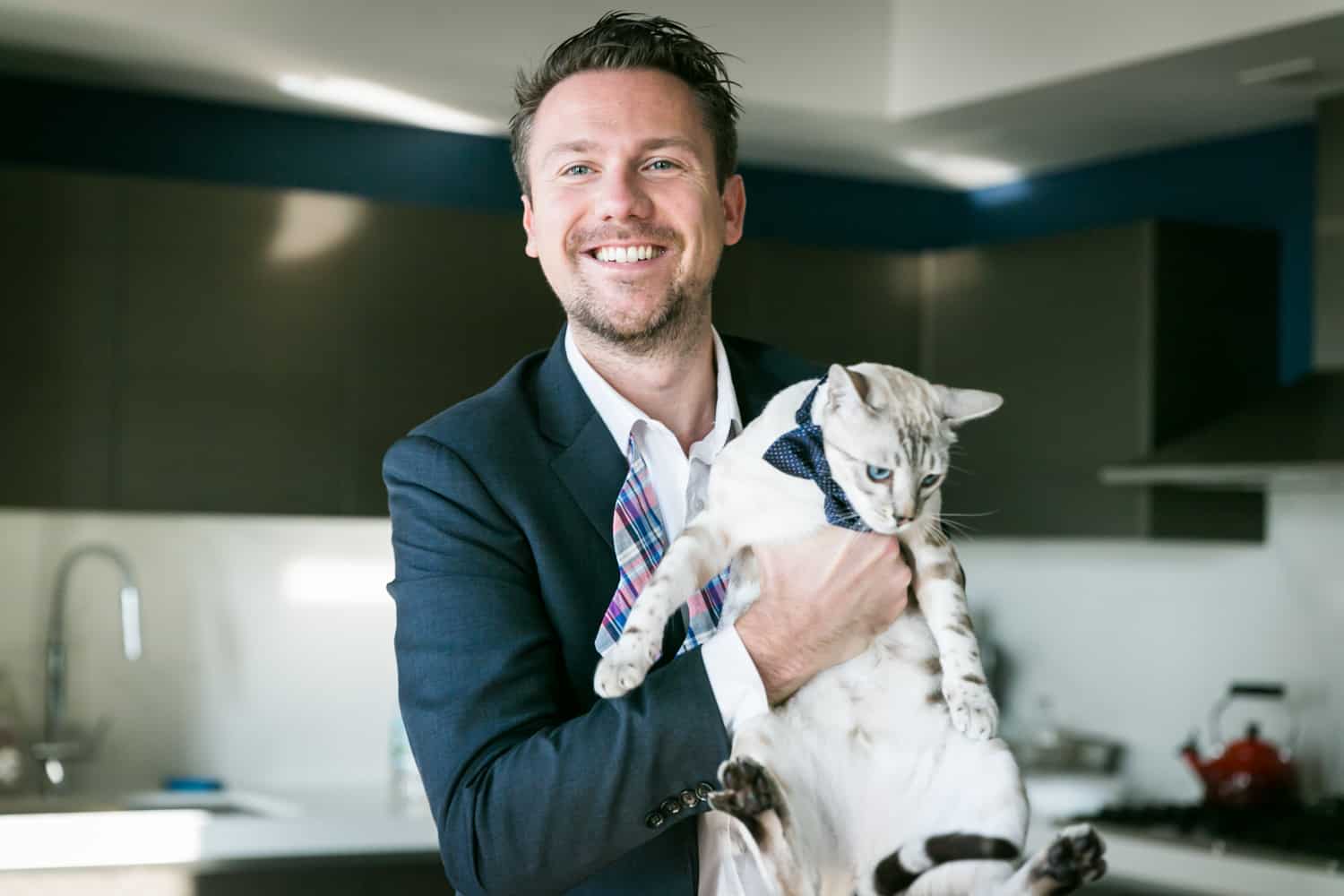 Groom holding cat wearing bowtie for an article on tips for including your pet in your wedding