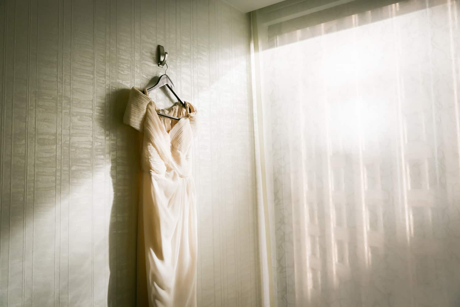 Wedding dress hanging on wall with rays of sun