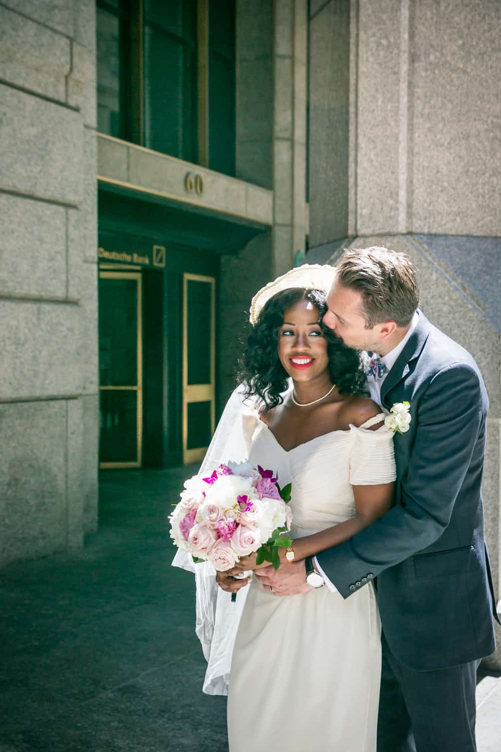 Groom kissing bride on side of head on Wall Street