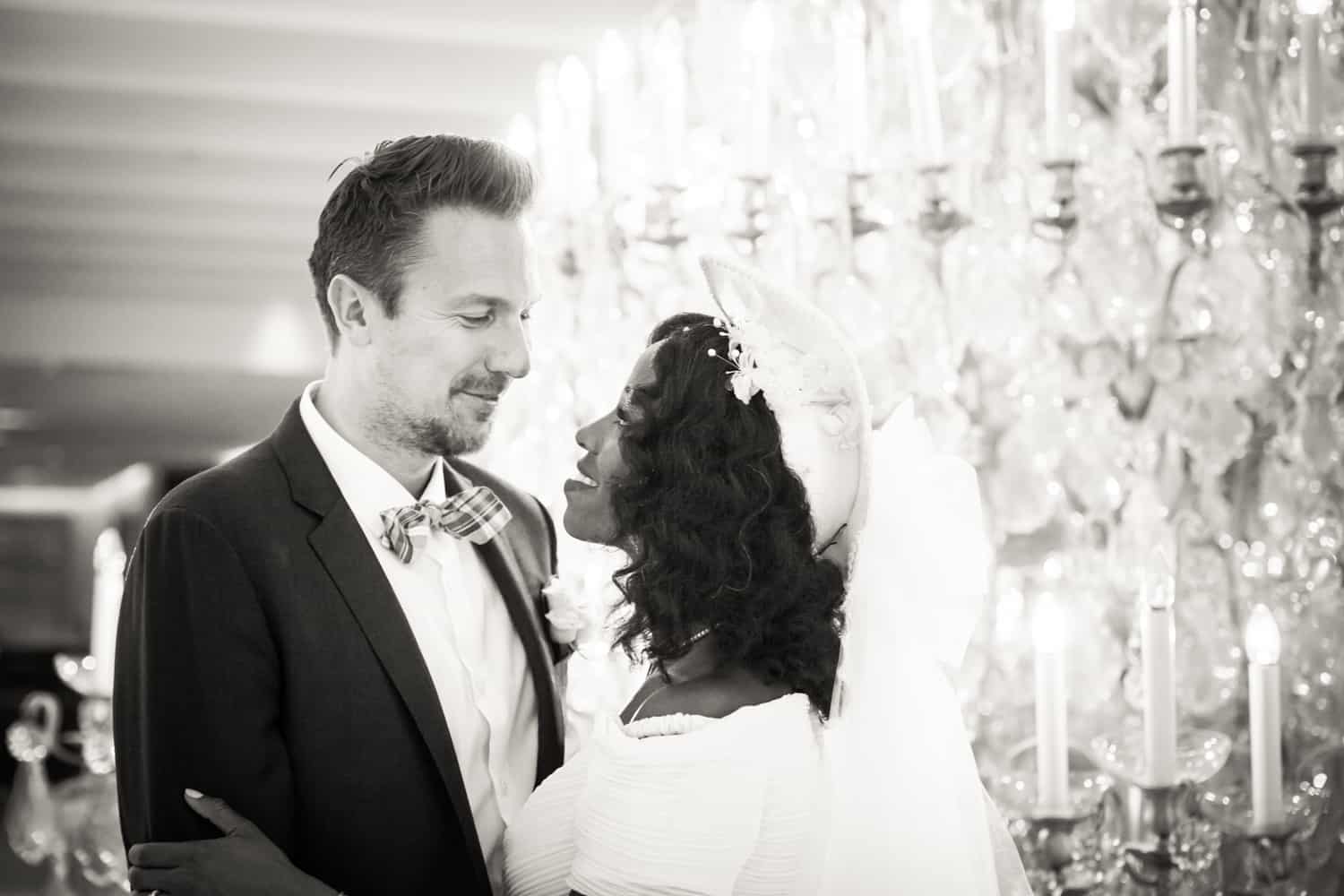 Black and white photo of bride and groom in front of chandelier