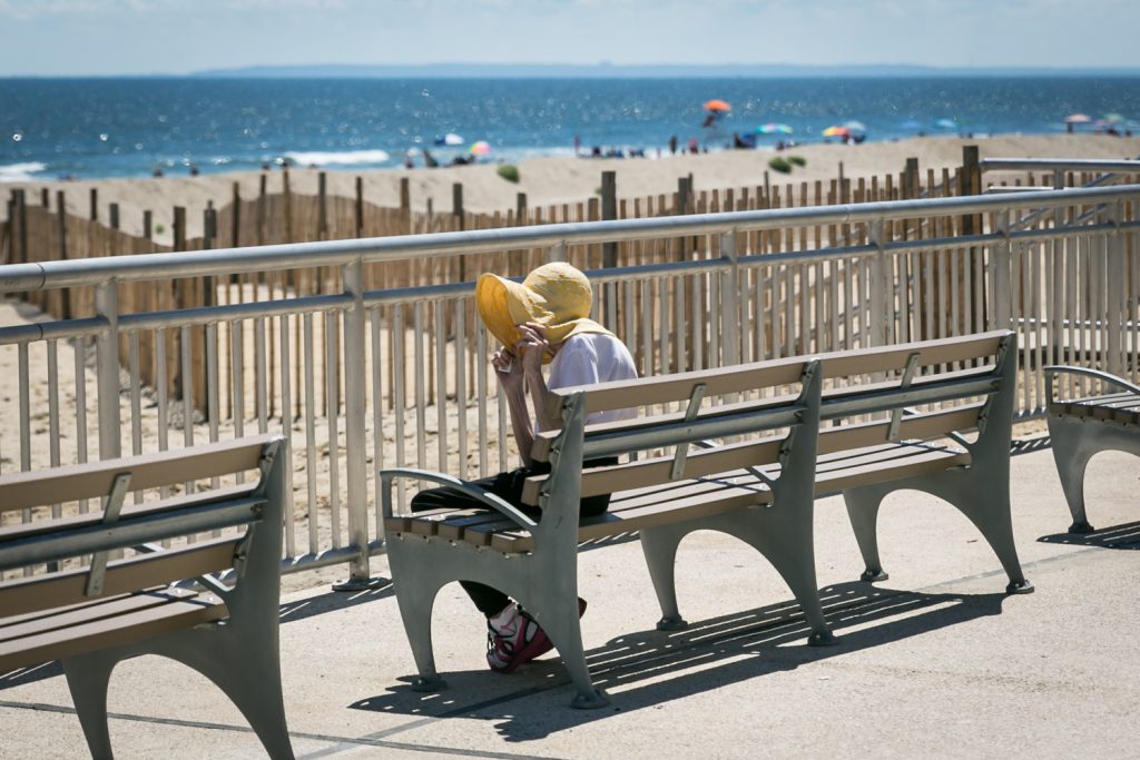 Woman holding onto hat on Far Rockaway beach boardwalk