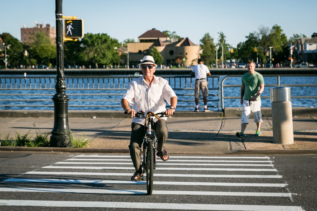 Old man wearing white hat and riding bicycle in crosswalk in Sheepshead Bay, Brooklyn