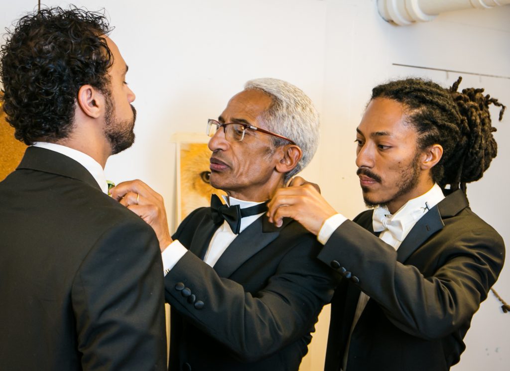 Groom adjusting collar of father, who is adjusting collar of best man 