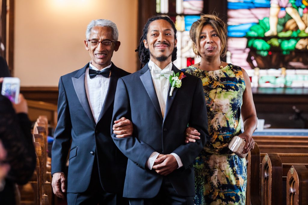 Groom walking down aisle of church with both parents