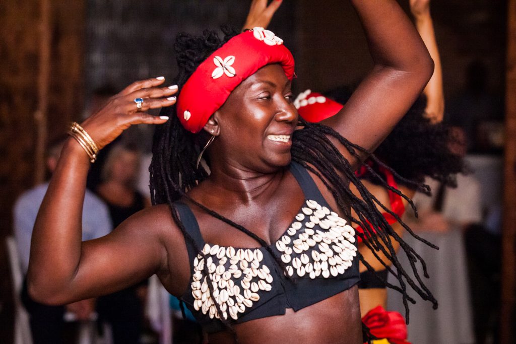 Woman in African costume dancing with arms raised at a DUMBO Loft wedding