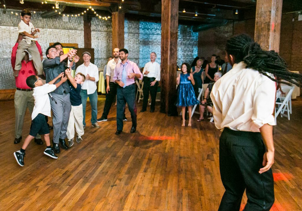 Male guests jumping to catch bow tie thrown by groom at a DUMBO Loft wedding